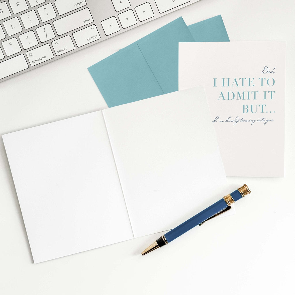 Hate to Admit It card by Blú Rose shown open with blank interior, blue envelope and pen on a white desk