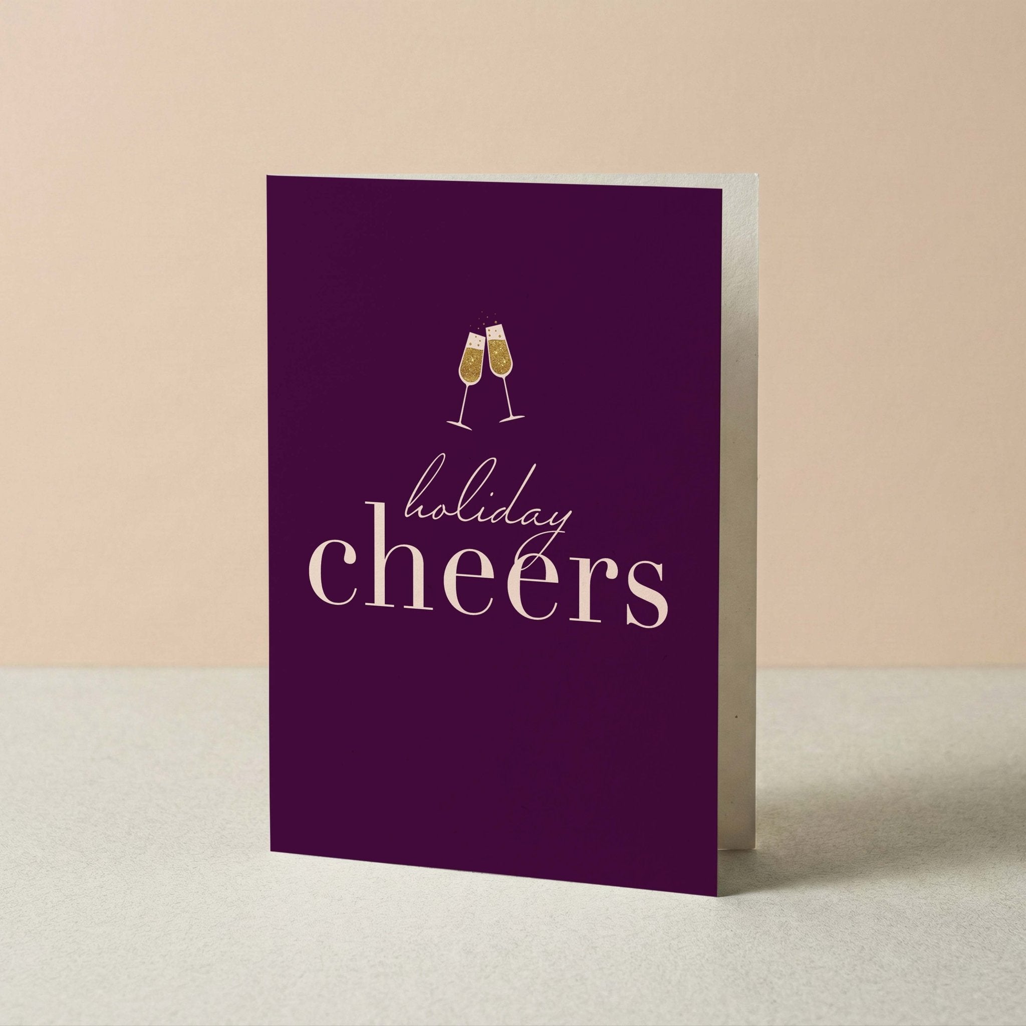 Holiday Cheers Christmas card by Blú Rose standing upright, plum card with champagne cheers design on a neutral background