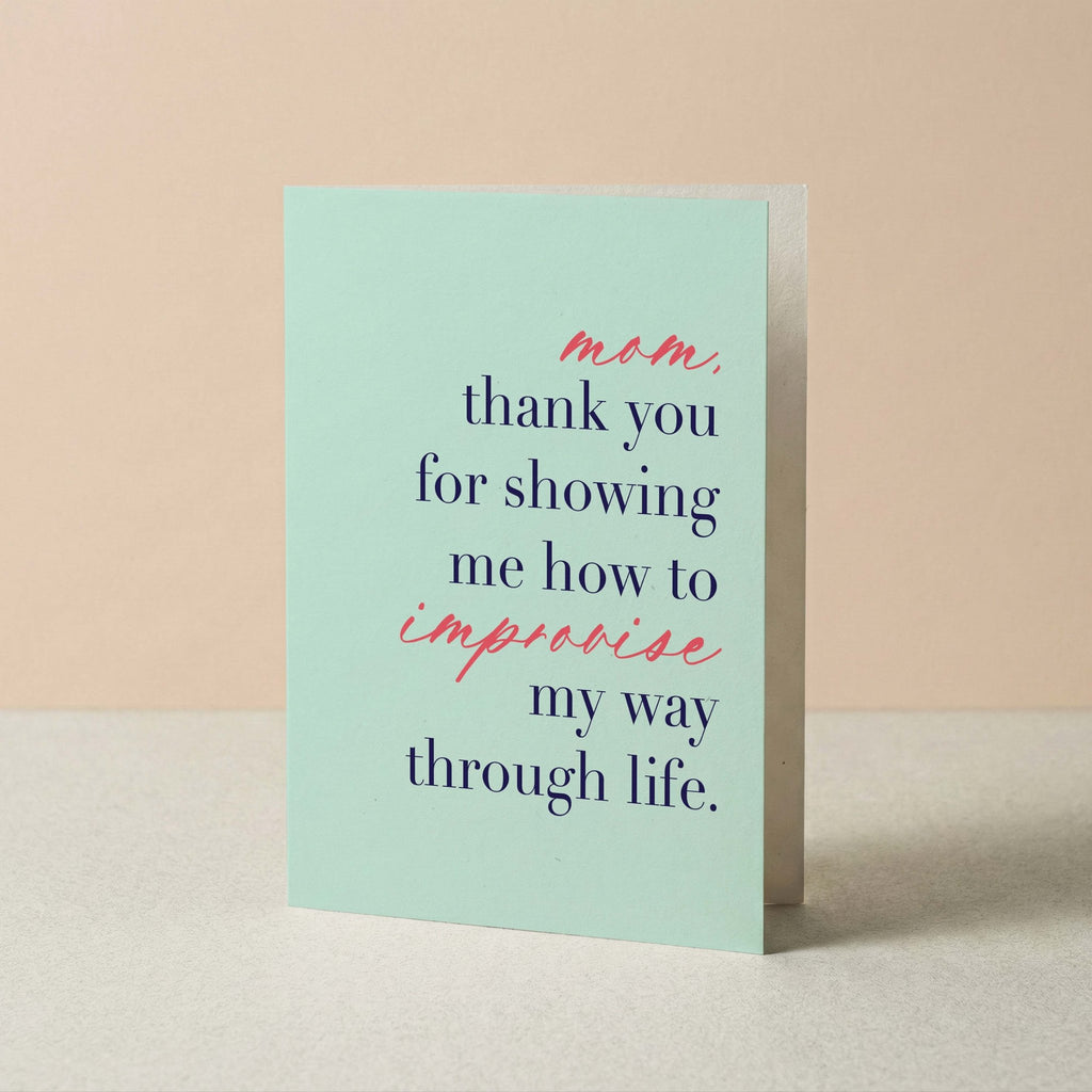 A mint green greeting card with a humorous quote for Mom, displayed standing upright on a light surface against a warm beige background.