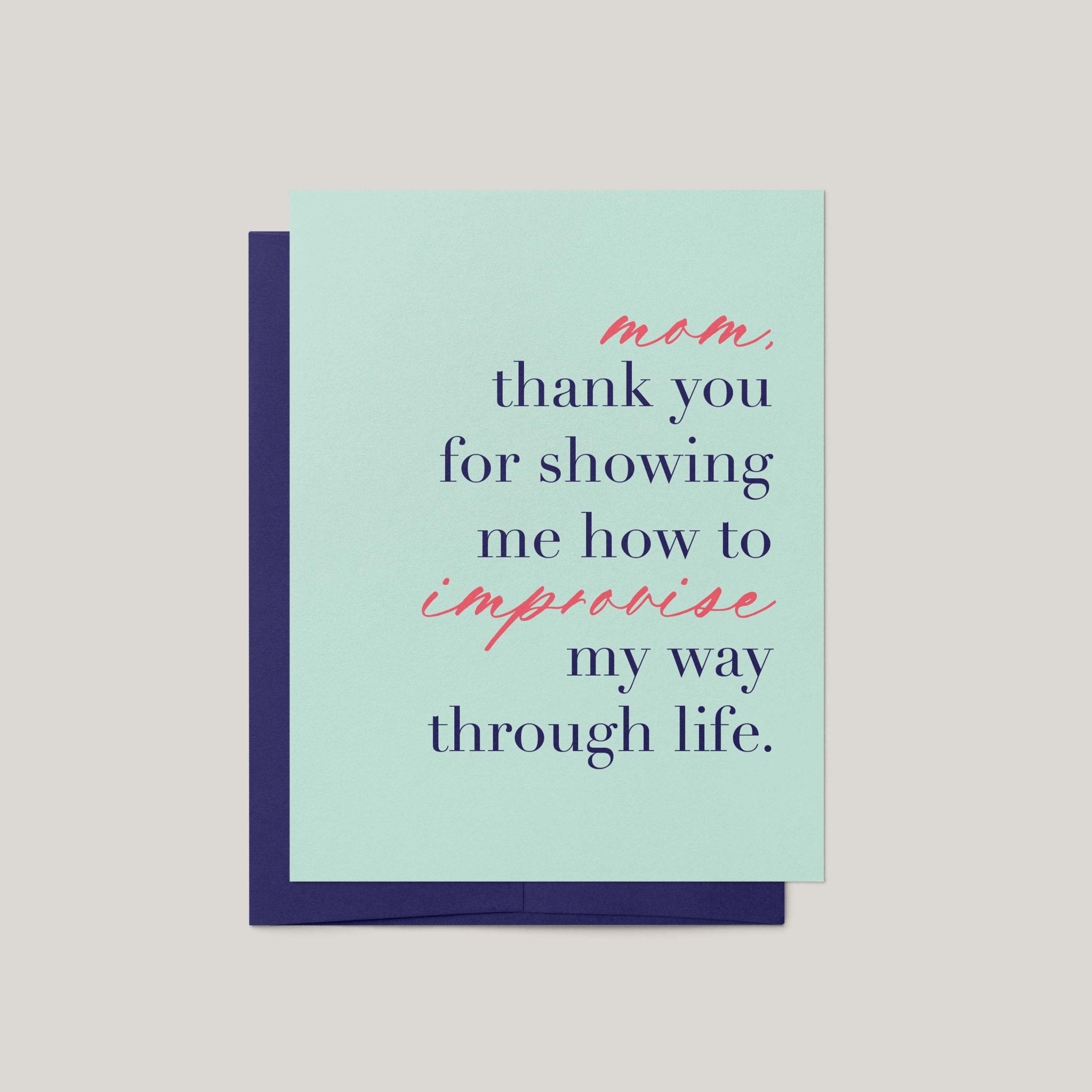A greeting card with a light mint green front and a dark navy envelope behind it, featuring the printed message: 'mom, thank you for showing me how to improvise my way through life.' in navy and coral script.