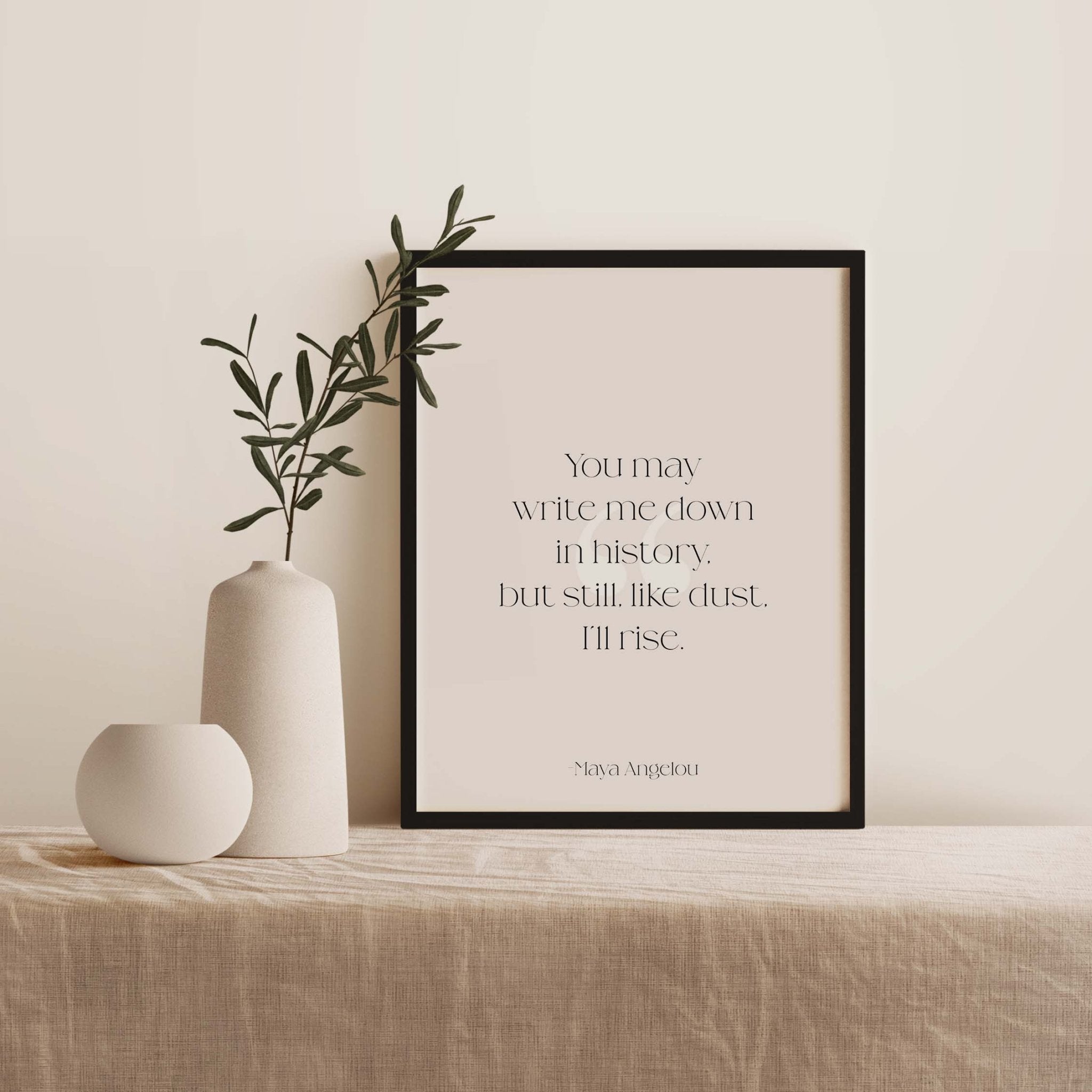 Framed artwork with a quote by Maya Angelou on a table with decorative vases and plants.