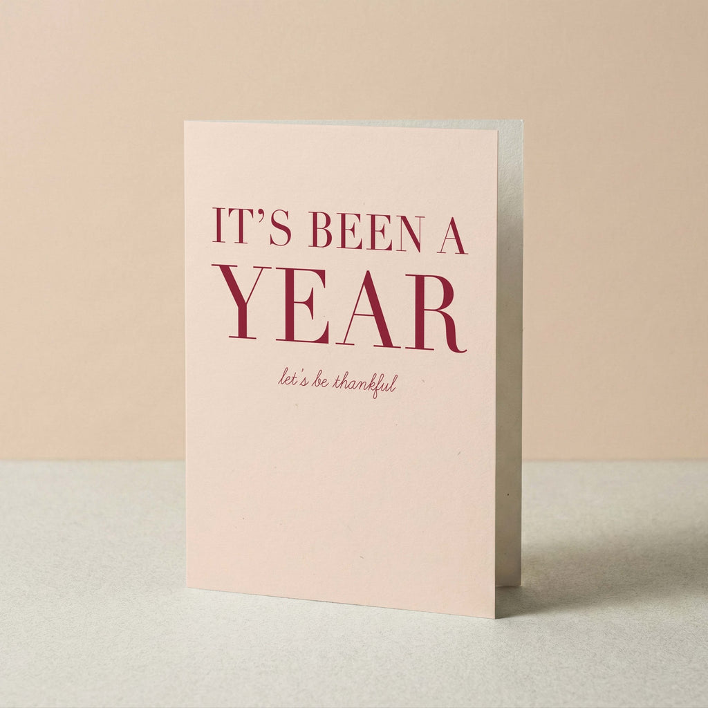 It's Been a Year gratitude card by Blú Rose standing upright, blush card with burgundy typography on a neutral background