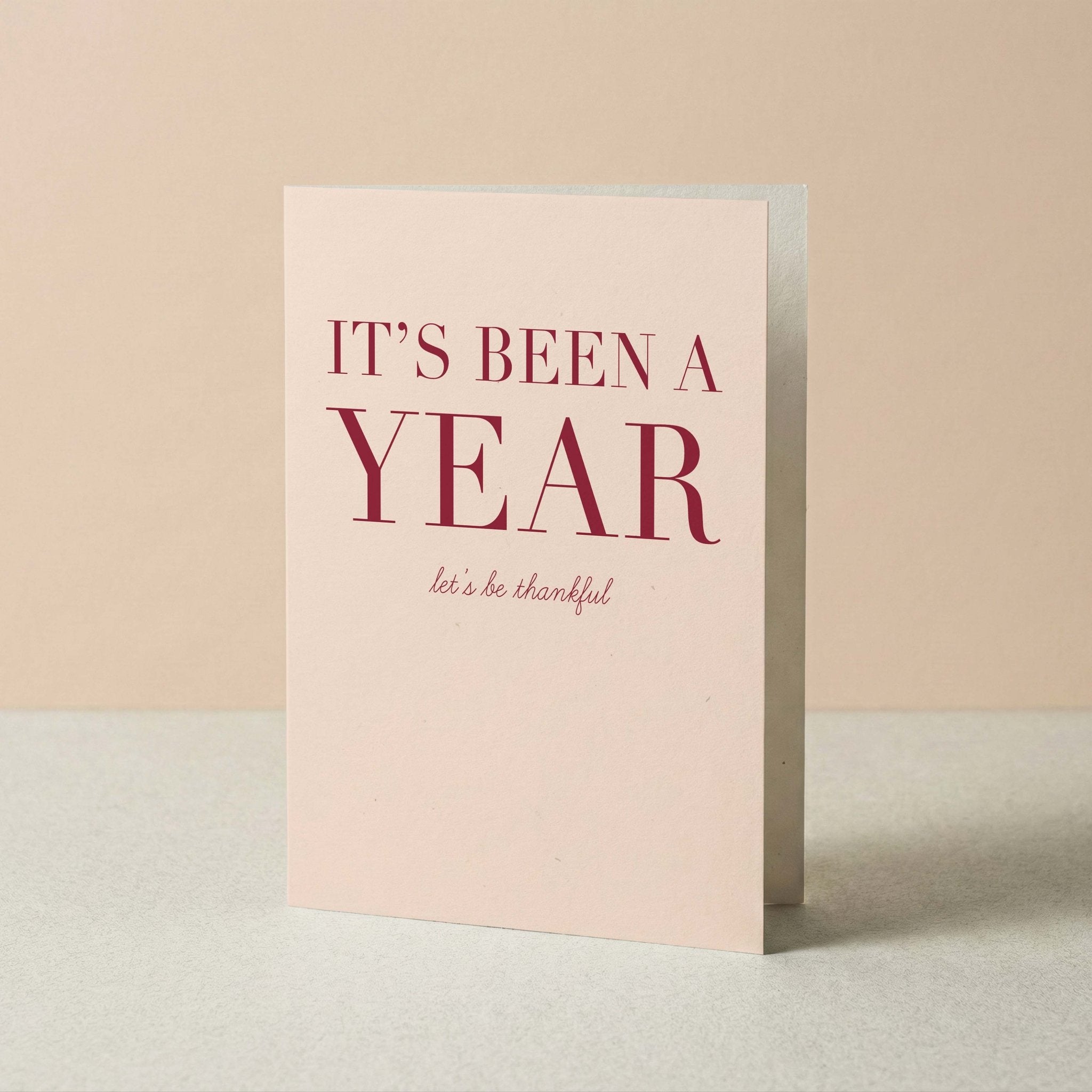It's Been a Year gratitude card by Blú Rose standing upright, blush card with burgundy typography on a neutral background