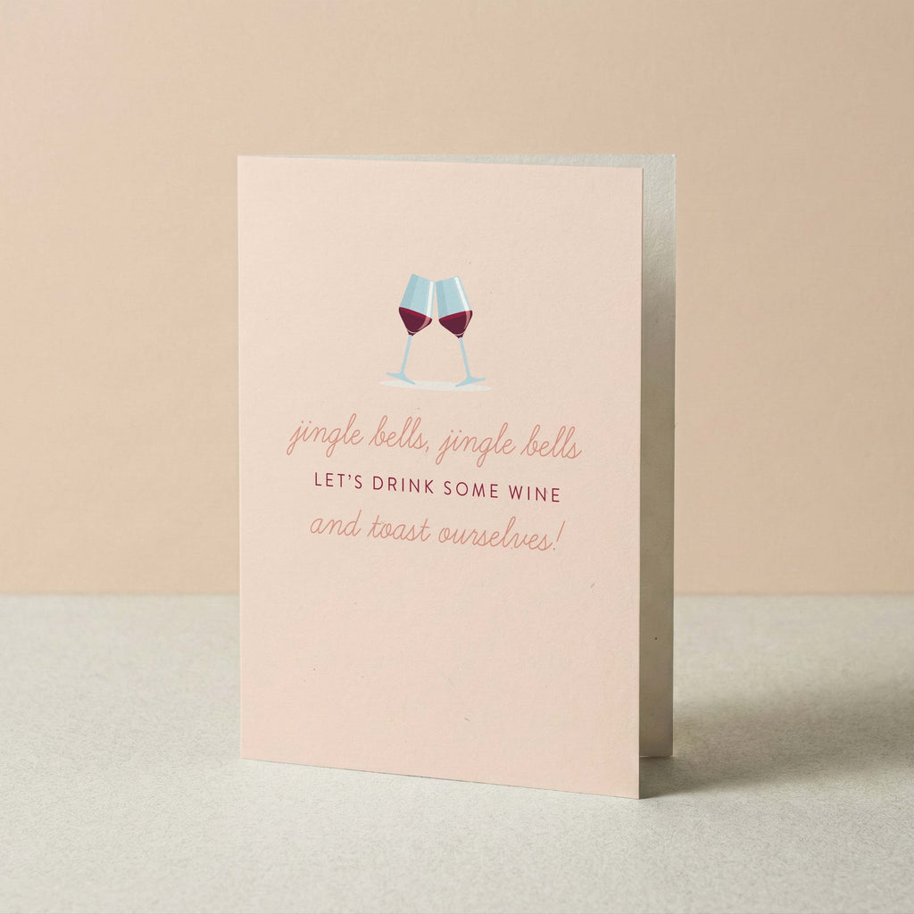 Jingle Bells & Wine Christmas greeting card by Blú Rose standing upright, blush card with wine glasses illustration on a neutral background