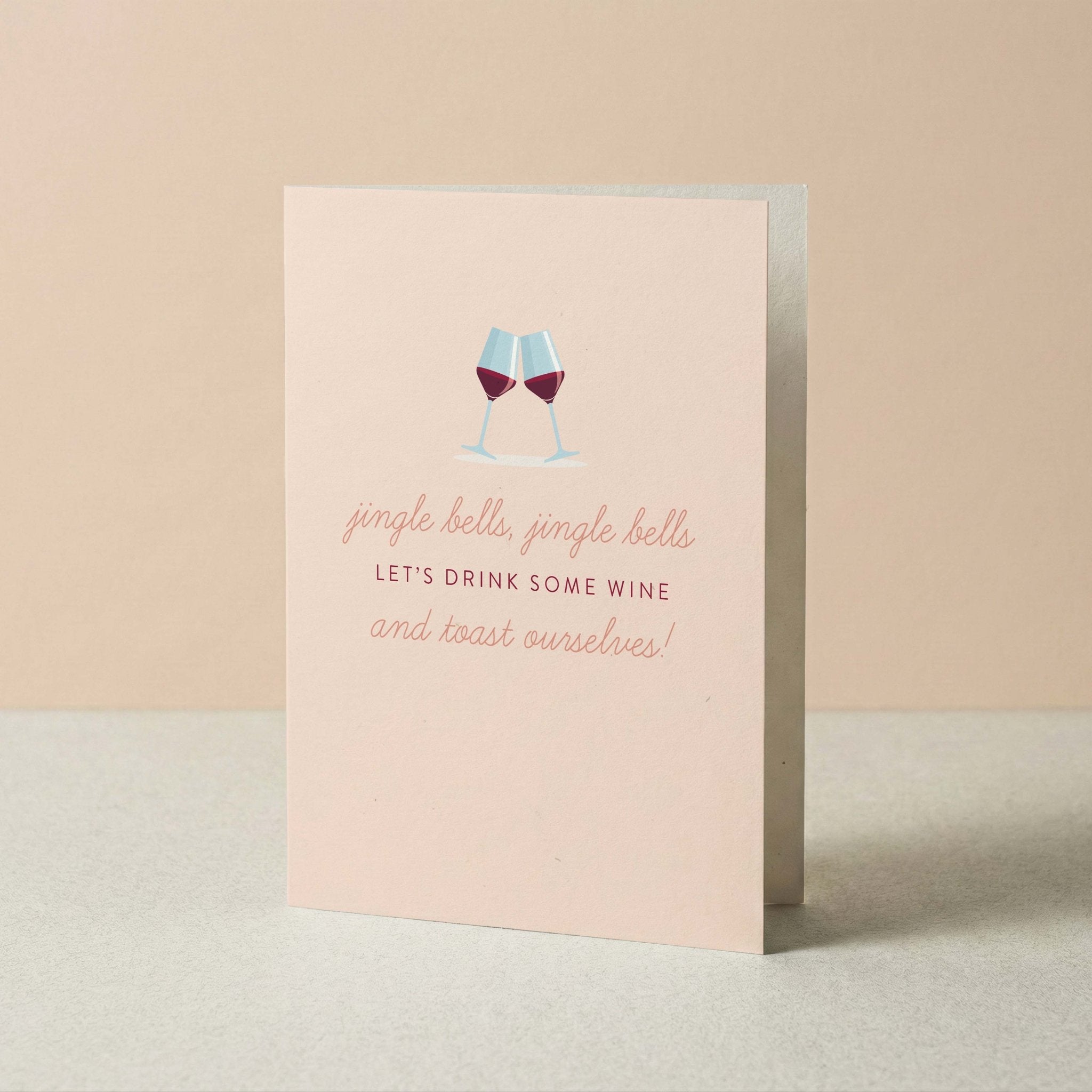 Jingle Bells & Wine Christmas greeting card by Blú Rose standing upright, blush card with wine glasses illustration on a neutral background