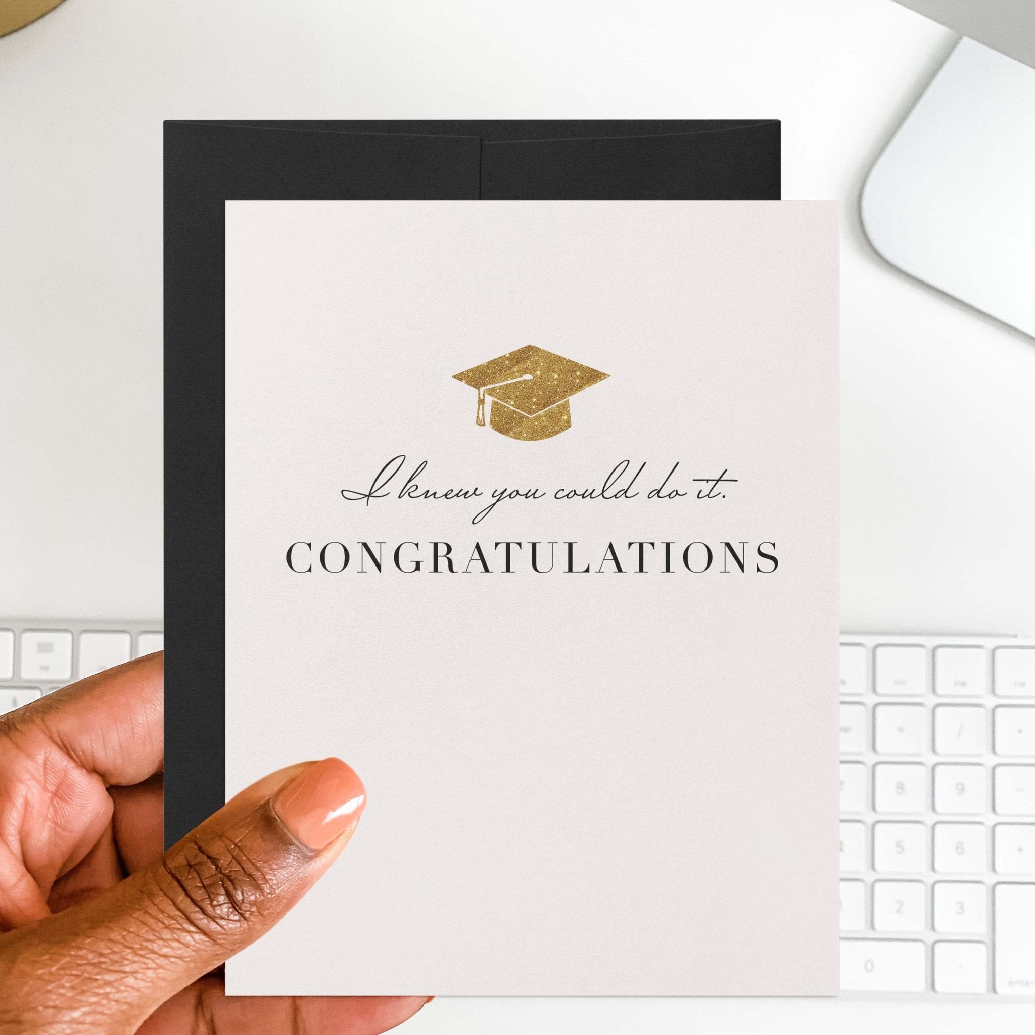 Knew You Could Do It graduation card by Blú Rose held in hand over a white desk with keyboard and black envelope