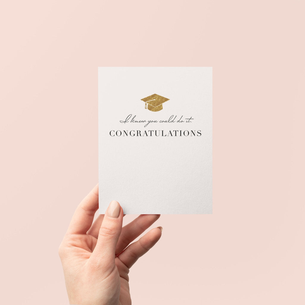 Knew You Could Do It graduation greeting card by Blú Rose held in hand against a neutral off-white background