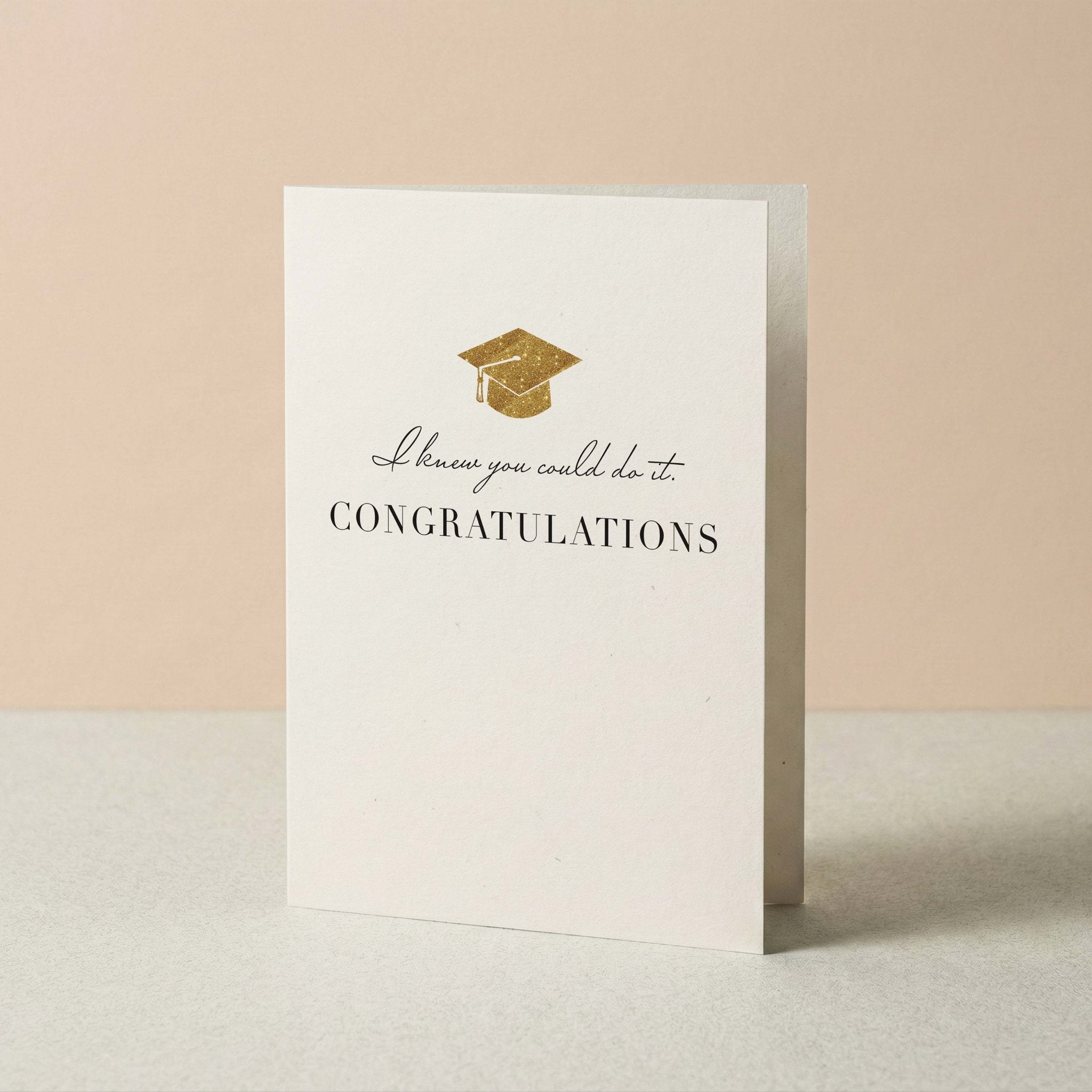 Knew You Could Do It graduation card by Blú Rose standing upright, ivory card with grad cap design on a neutral background