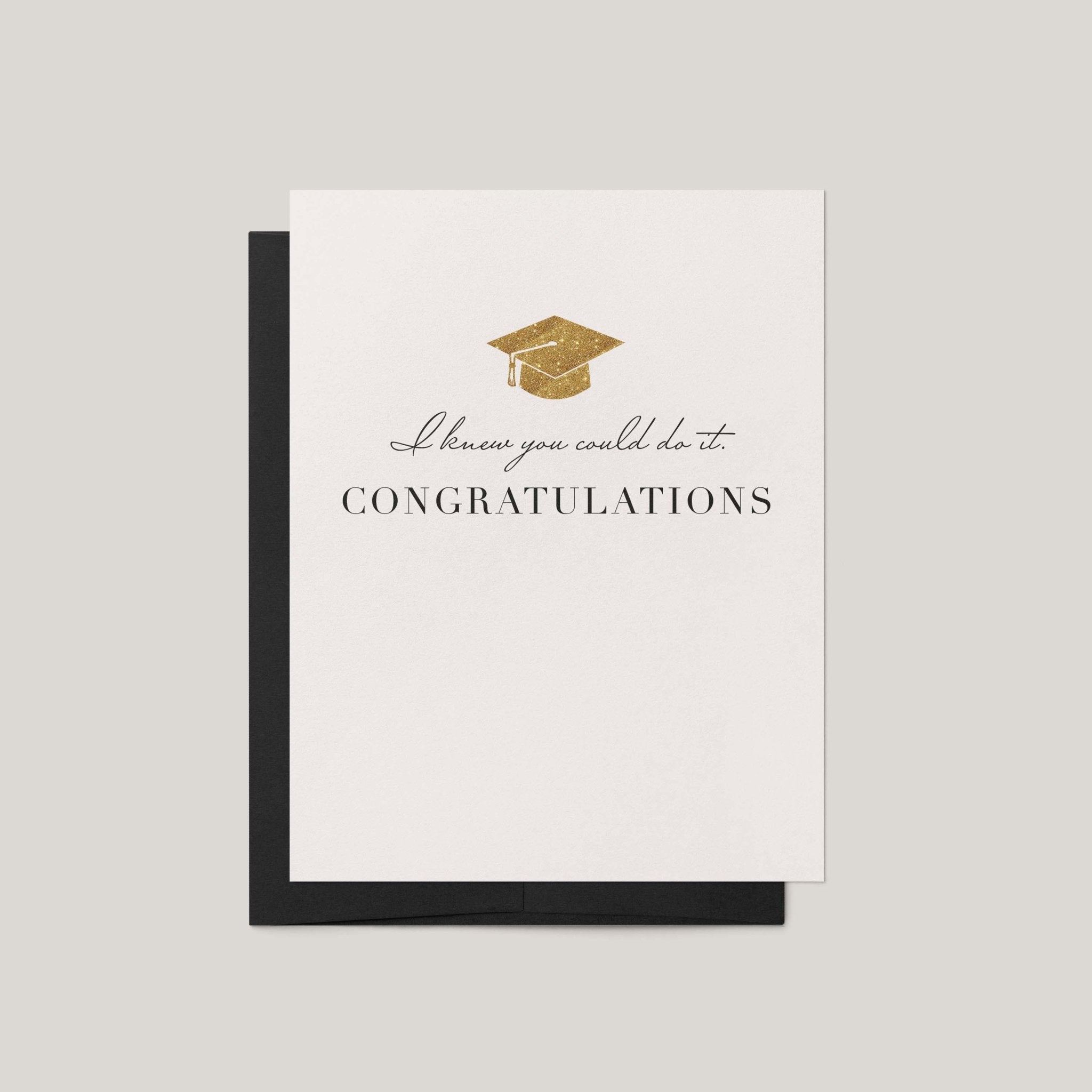 Knew You Could Do It graduation greeting card by Blú Rose, ivory card with gold graduation cap and congratulations text, shown with black envelope