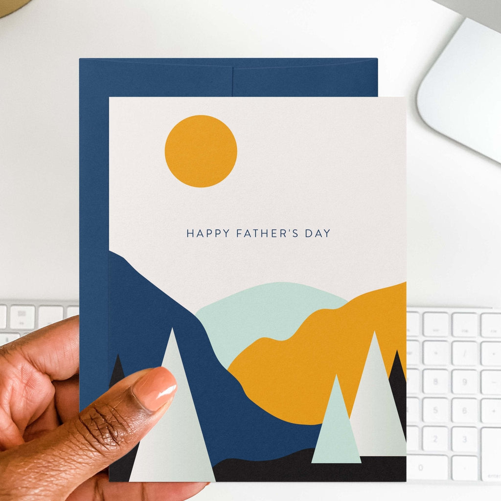Landscape Father's Day card by Blú Rose held in hand over a white desk with keyboard and navy envelope