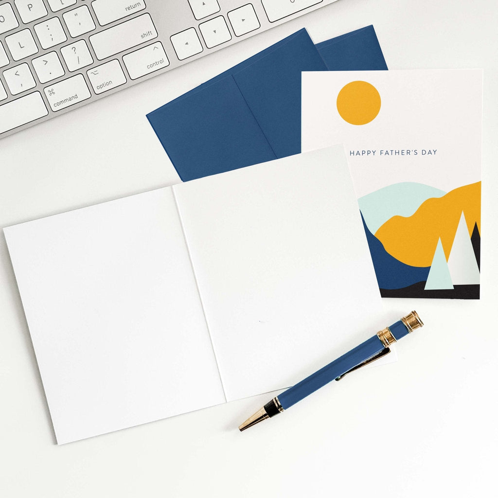 Landscape Father's Day card by Blú Rose shown open with blank interior, navy envelope and pen on a white desk