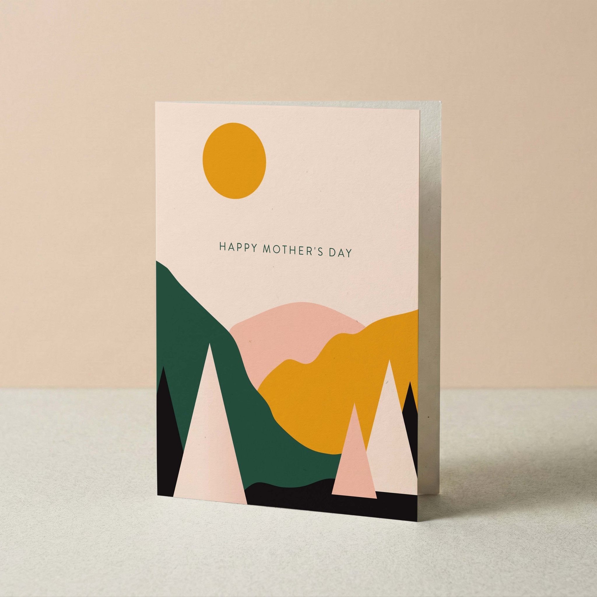 A Mother's Day greeting card with a minimalist geometric mountain landscape design in shades of green, pink, yellow, and black on a cream background, with a yellow sun and the text 'HAPPY MOTHER'S DAY'.