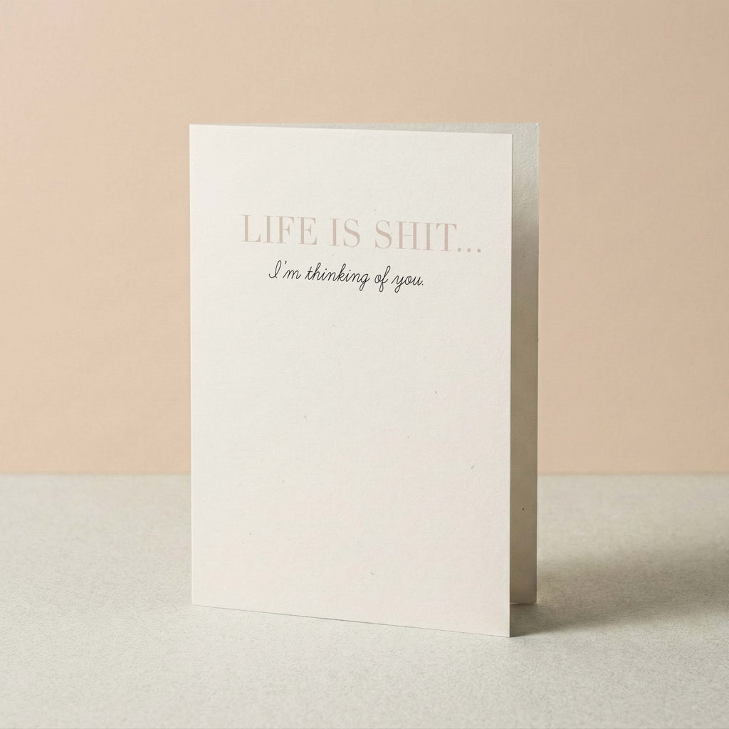 Life Is Shit funny thinking of you card by Blú Rose standing upright, ivory card with taupe serif text on a neutral background