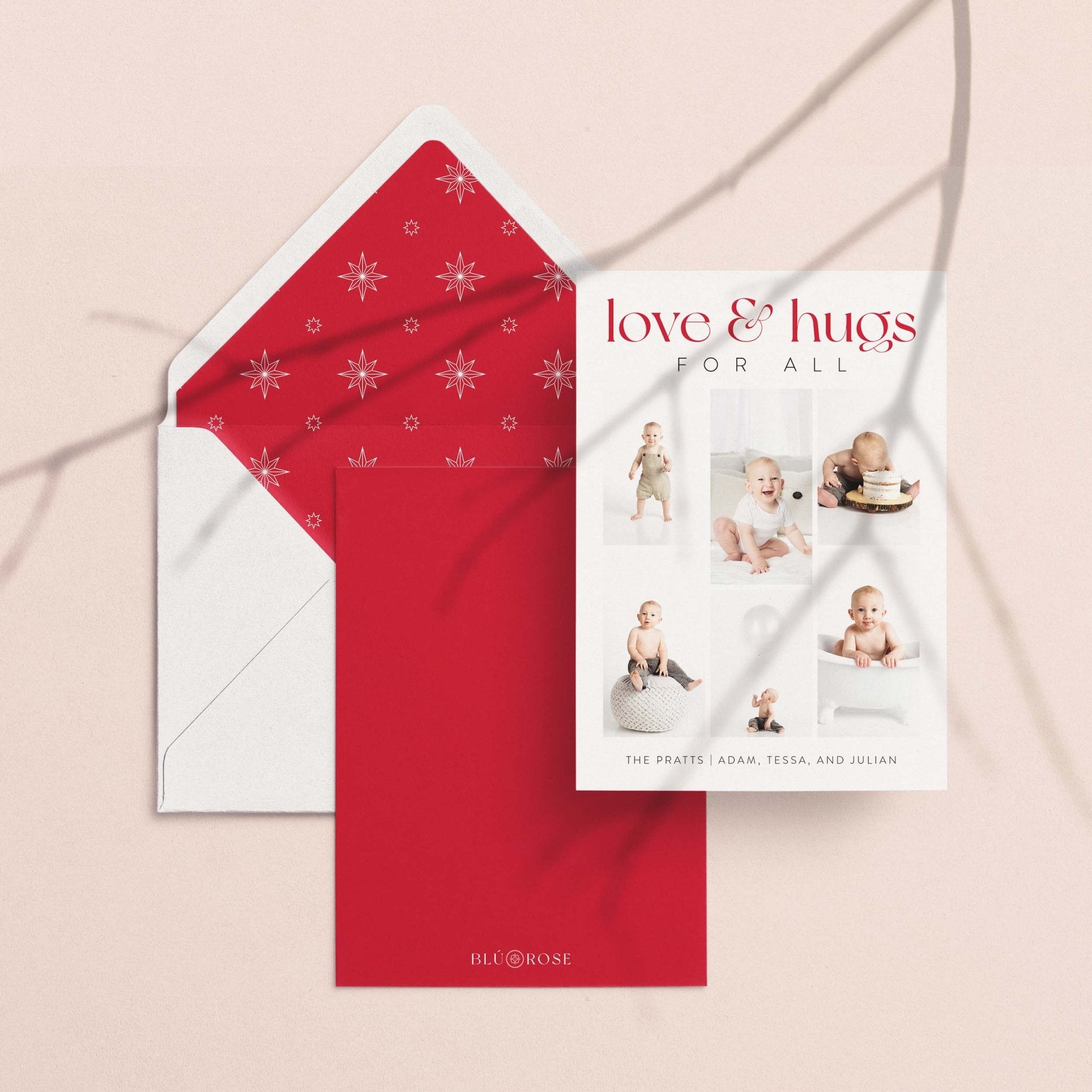 Love + Hugs card with its red snowflake envelope liner styled on a blush backdrop
