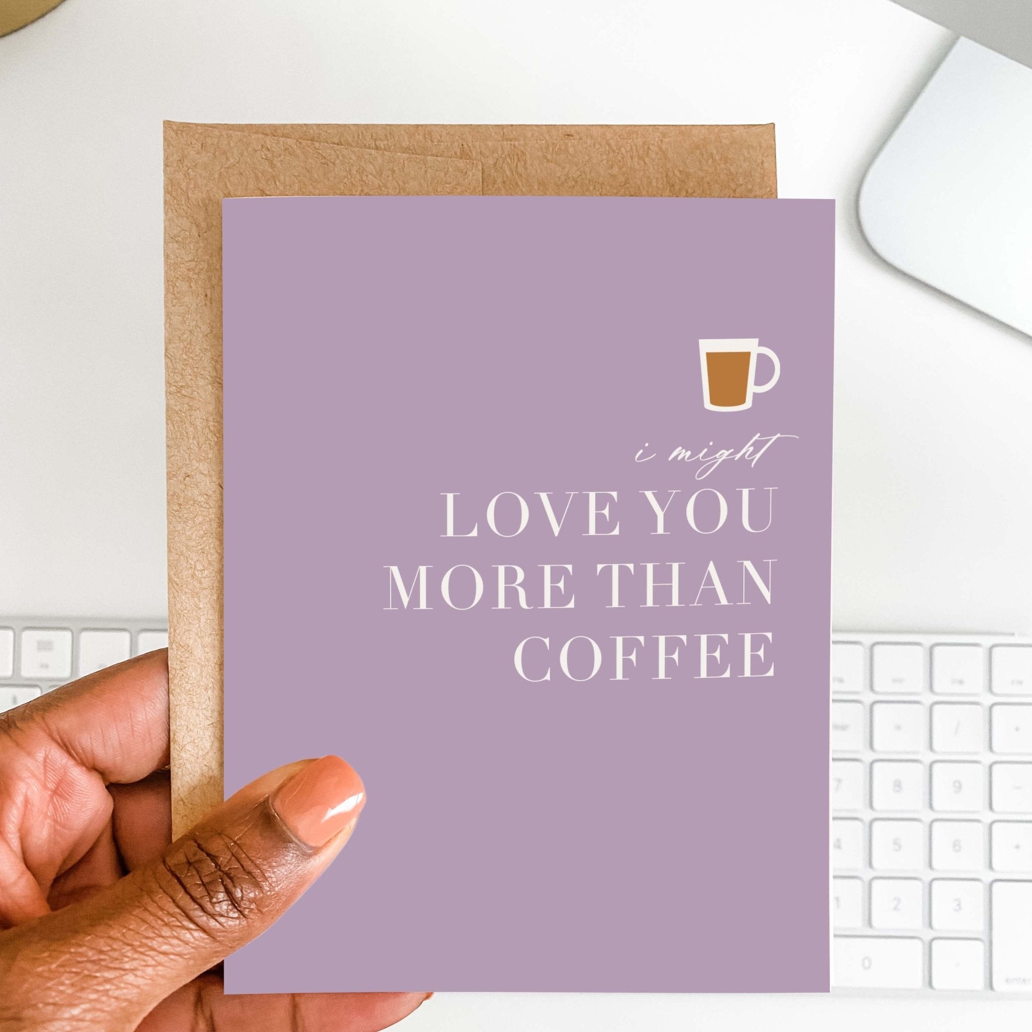 Love You More Than Coffee card by Blú Rose held in hand over a white desk with keyboard and kraft envelope