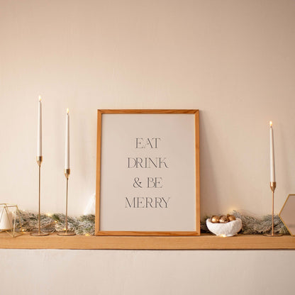Minimal Eat Drink & Be Merry art print displayed on a shelf with taper candles