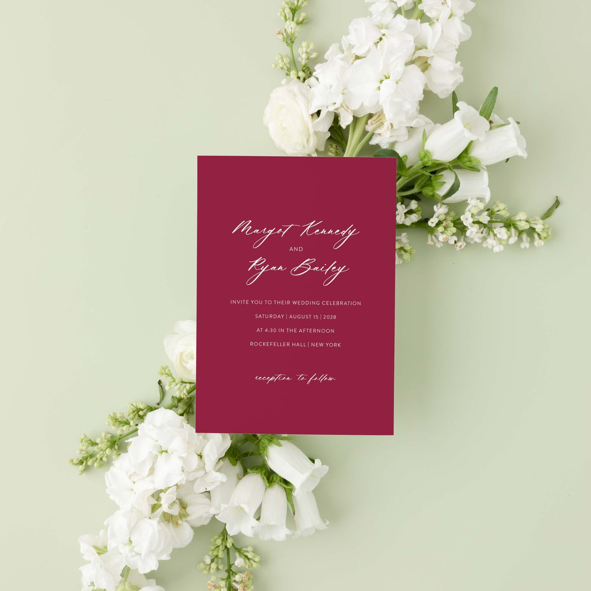 Minimalist Margot wedding invitation by Blú Rose, burgundy card with white script 'Margot & Ryan' names, styled on a sage background with white blooms