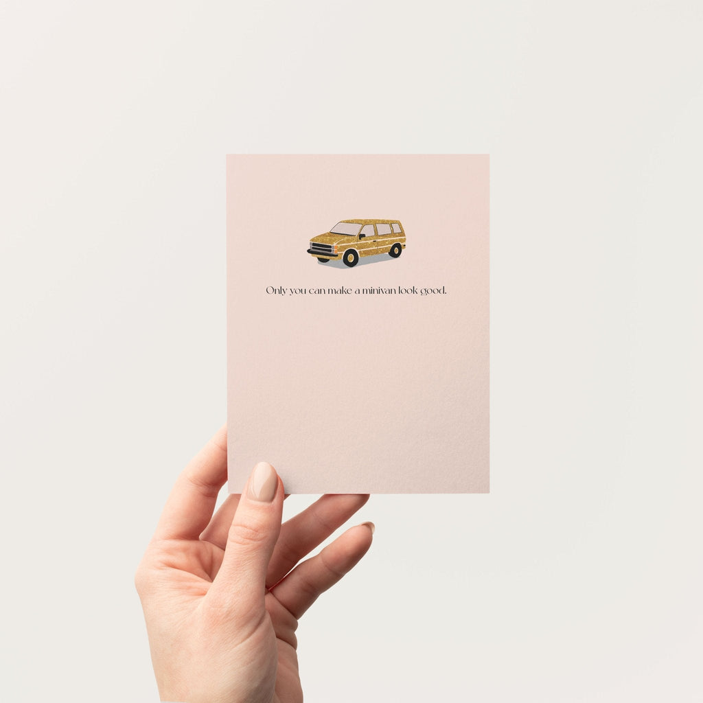 Hand holding a blush pink minivan greeting card against a neutral background, showing the card's front design.