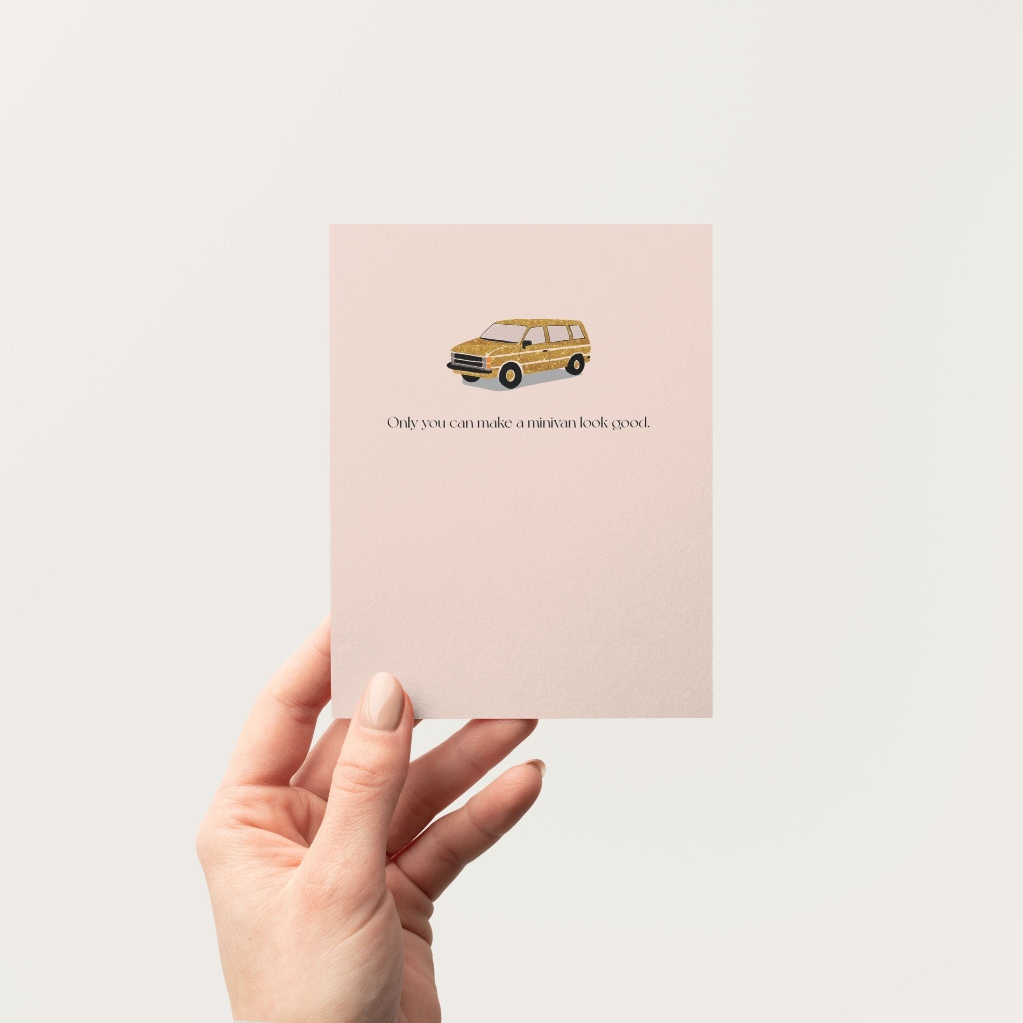 Hand holding a blush pink minivan greeting card against a neutral background, showing the card's front design.