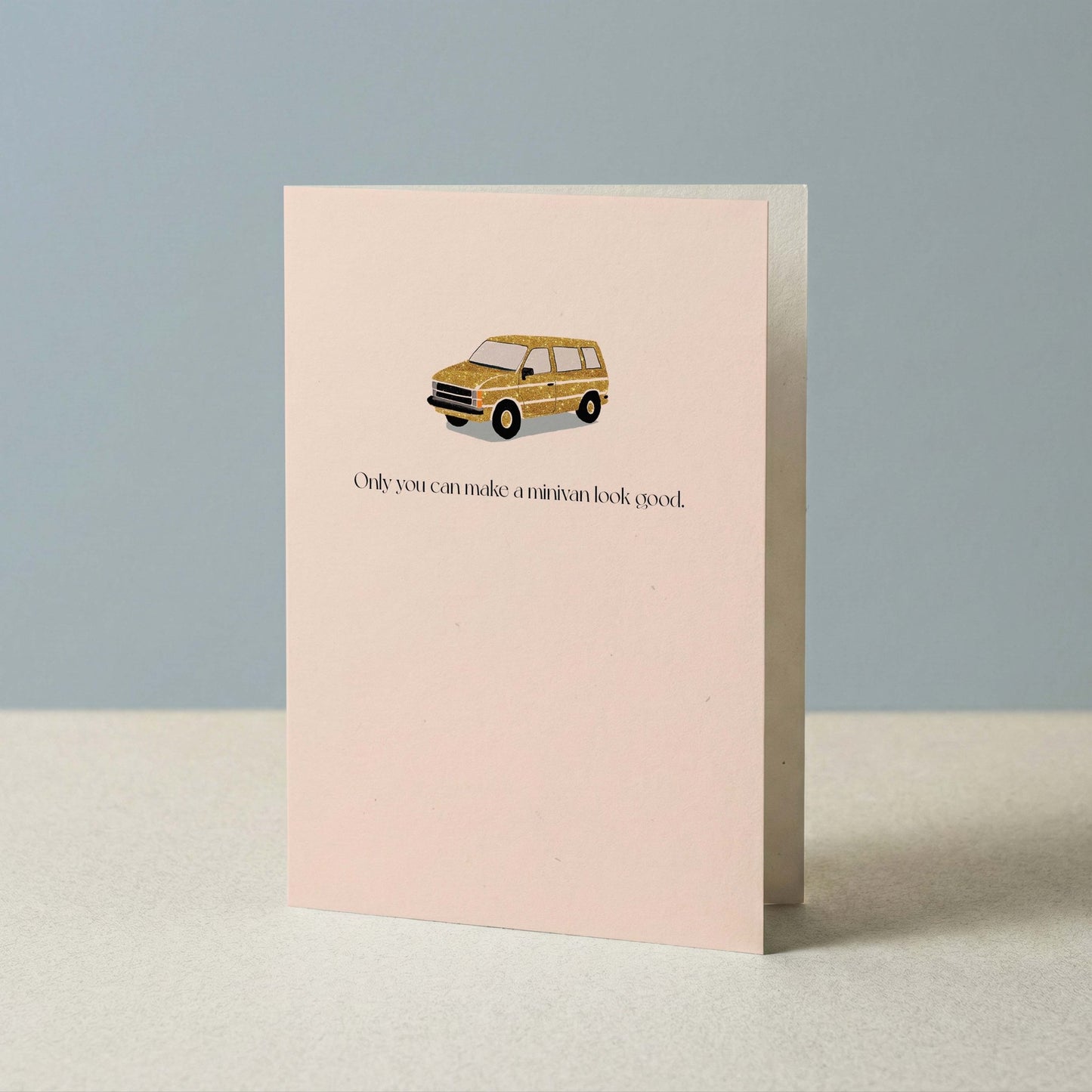 Blush pink minivan greeting card propped upright against a soft blue-gray background, showing the full card front.