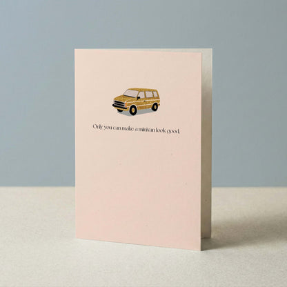 Blush pink minivan greeting card propped upright against a soft blue-gray background, showing the full card front.