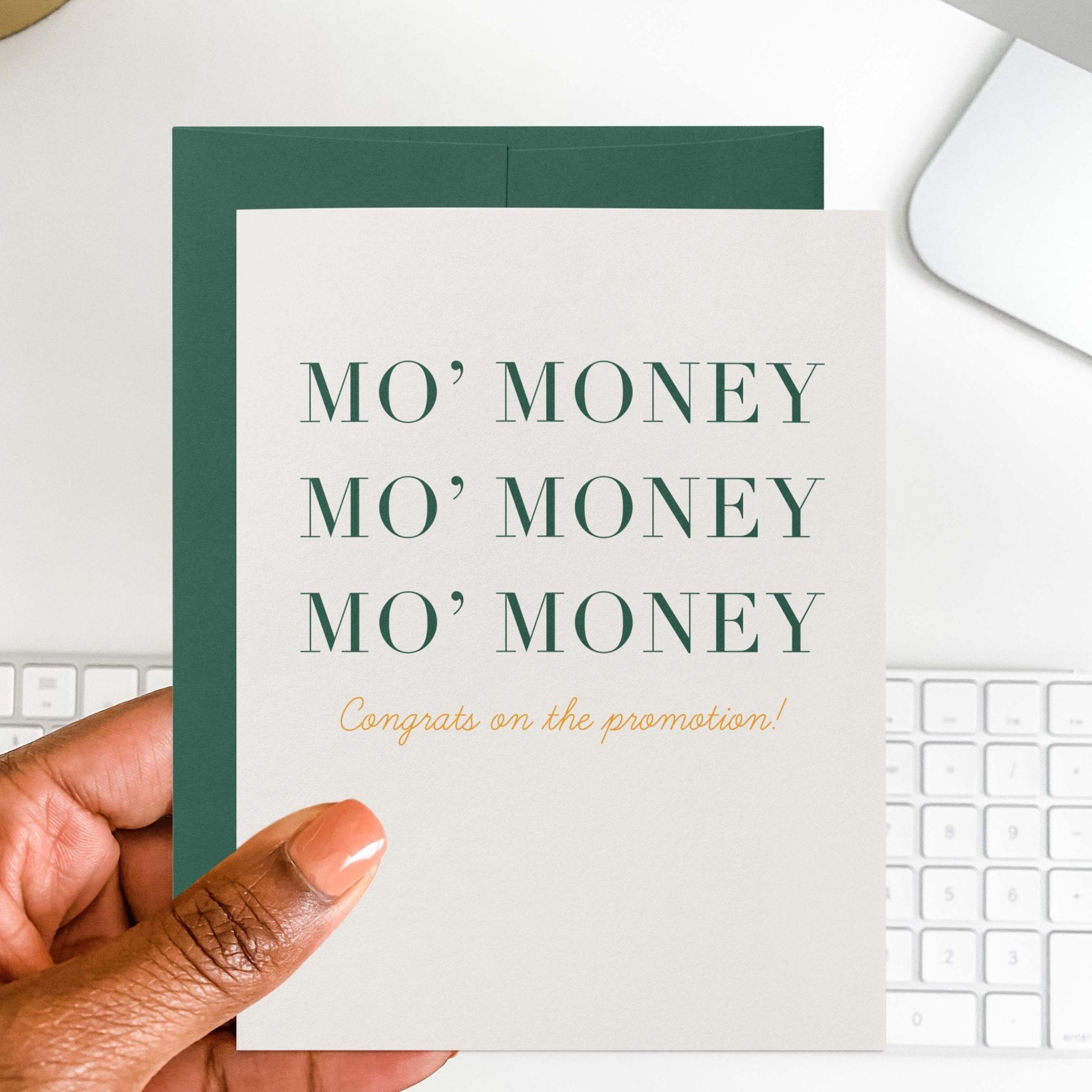 Mo' Money new job card by Blú Rose held in hand over a white desk with keyboard and green envelope
