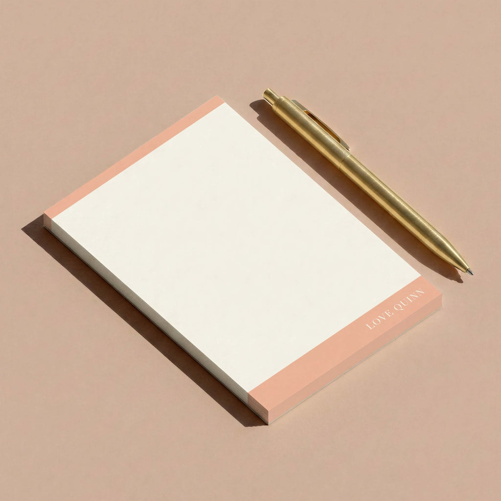 Mod Border personalized notepad by Blú Rose, peach color-block notepad styled at an angle with a gold pen on a mauve surface
