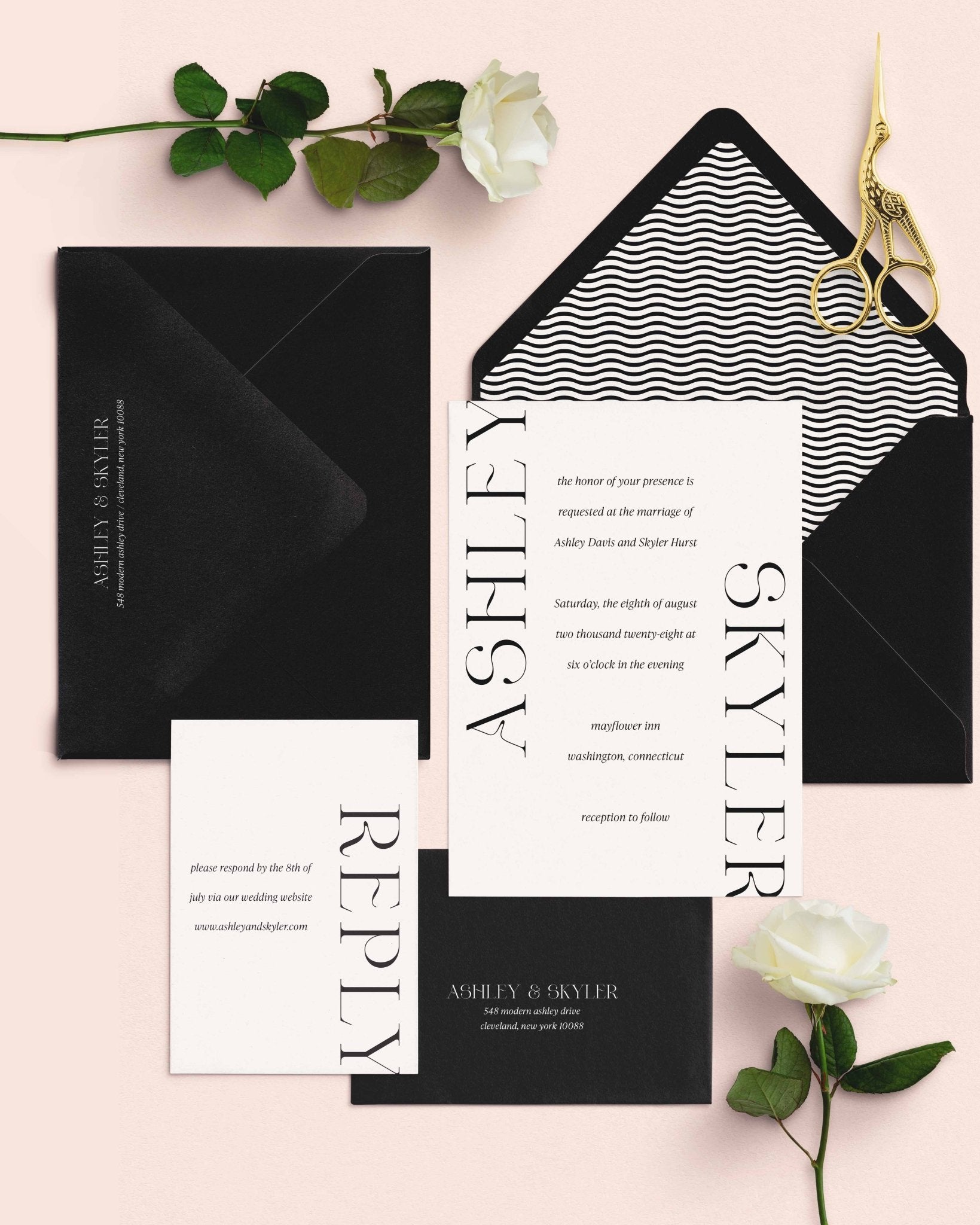 Modern Ashley wedding invitation suite by Blú Rose, invitation and reply card with oversized vertical names, styled on blush with black envelopes, a wave-pattern liner, roses, and gold scissors
