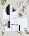 Modern Love wedding invitation suite by Blú Rose, minimalist invitation and reply card with a black side stripe, styled with black-and-white striped envelopes, ribbon, and a wax seal