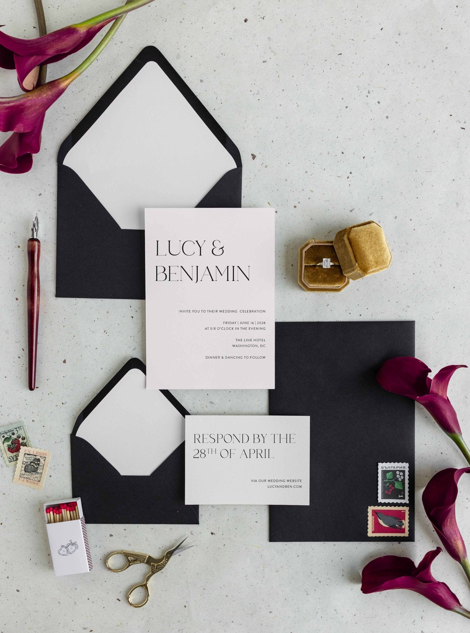 Modern Lucy wedding invitation suite by Blú Rose, minimalist invitation and reply card with large serif names, styled with black envelopes, deep red calla lilies, and a ring box