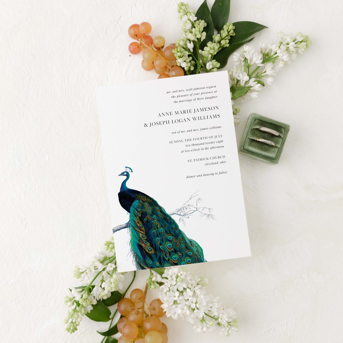 Modern Peacock wedding invitation by Blú Rose, white card with a vintage peacock illustration, styled with white lilacs, grapes, and wedding rings