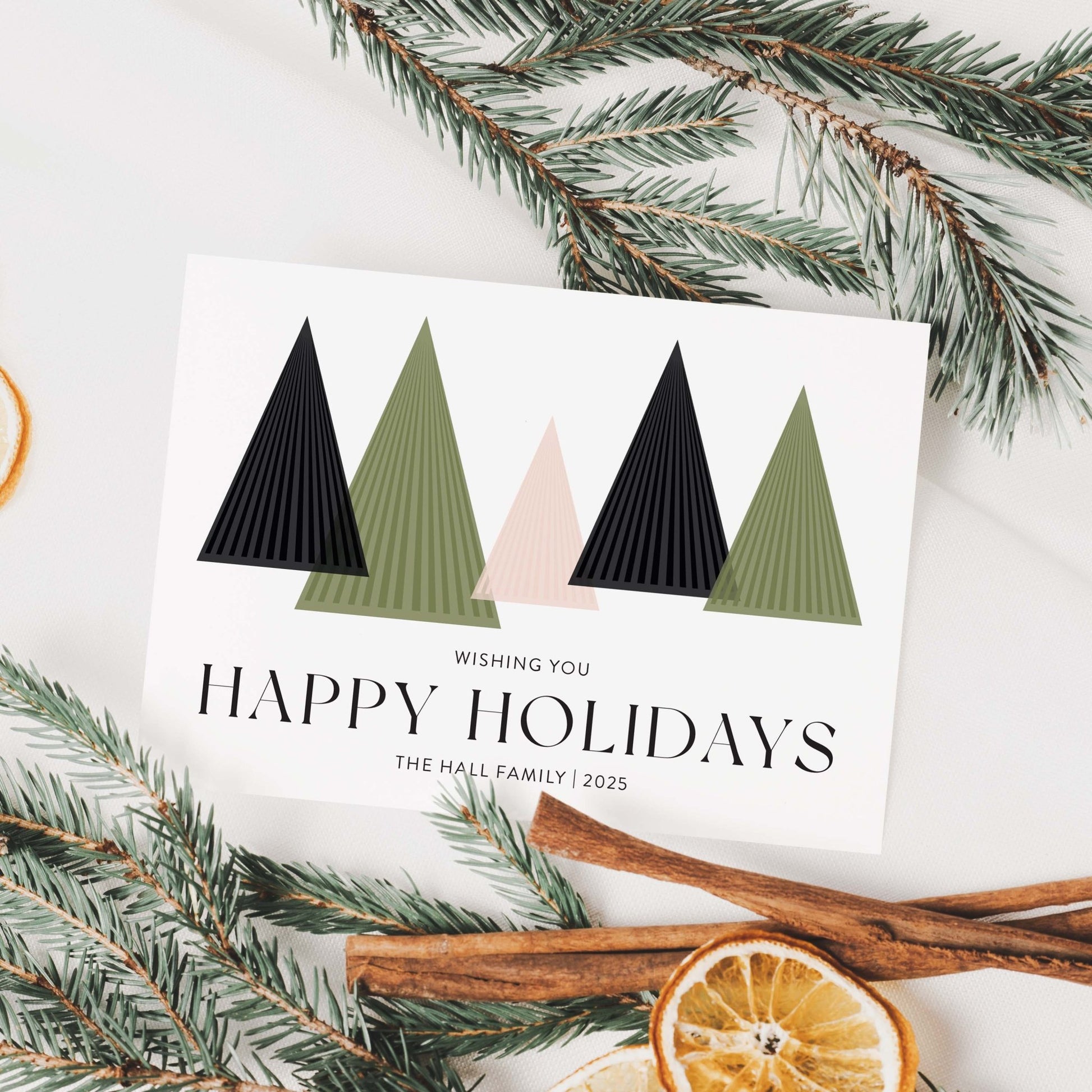 Styled holiday card with geometric trees surrounded by pine branches and dried oranges.