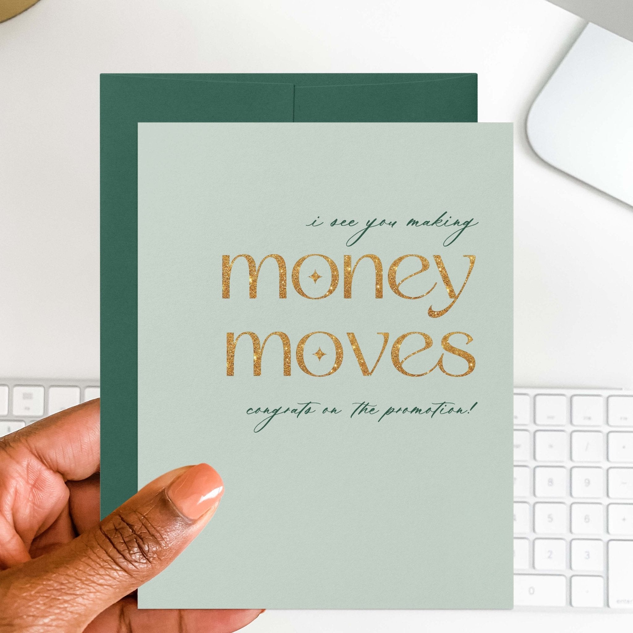 Money Moves new job card by Blú Rose held in hand over a white desk with keyboard and green envelope