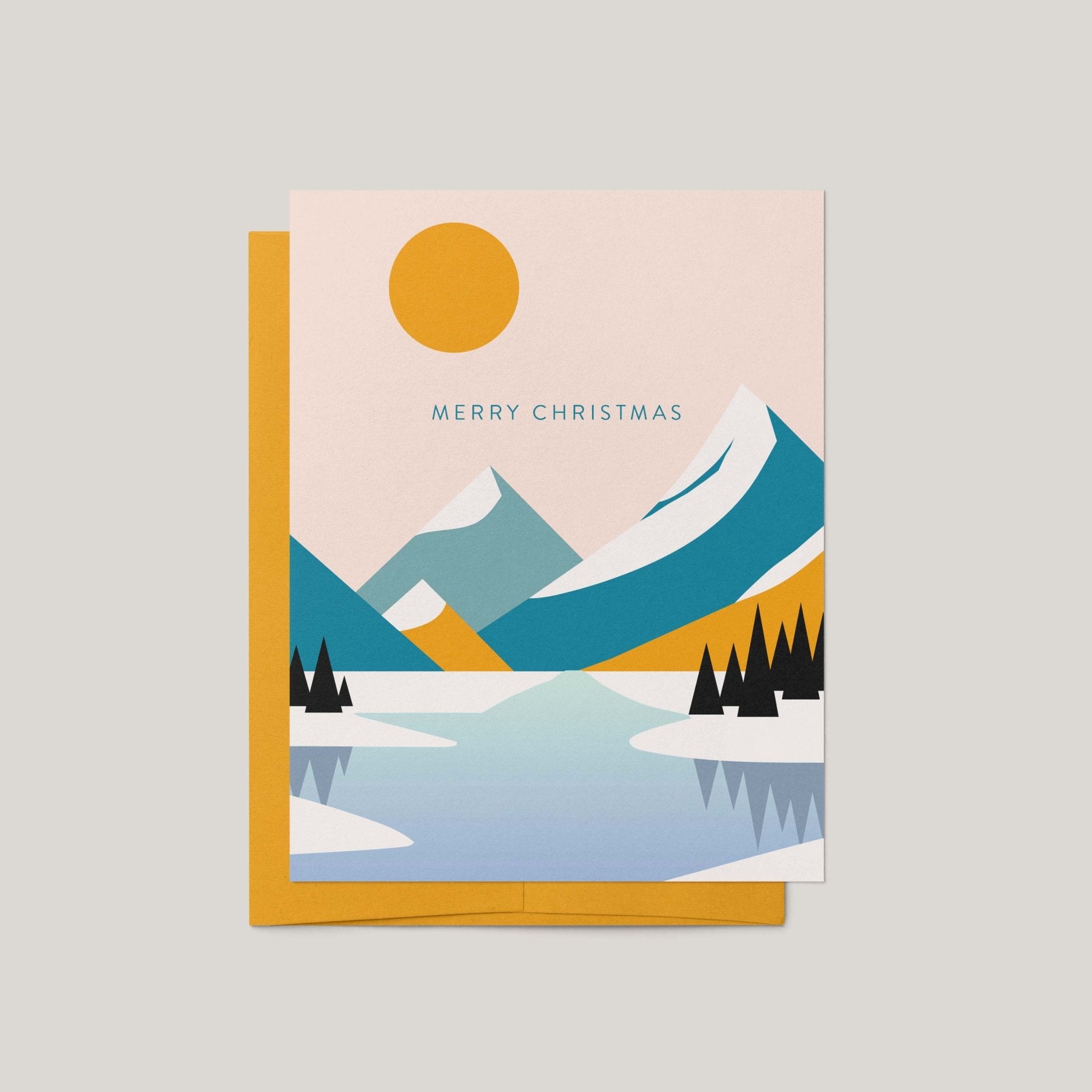 Mountain Landscape Christmas card by Blú Rose, modern minimalist snowy mountain and lake scene with Merry Christmas text, shown with marigold envelope