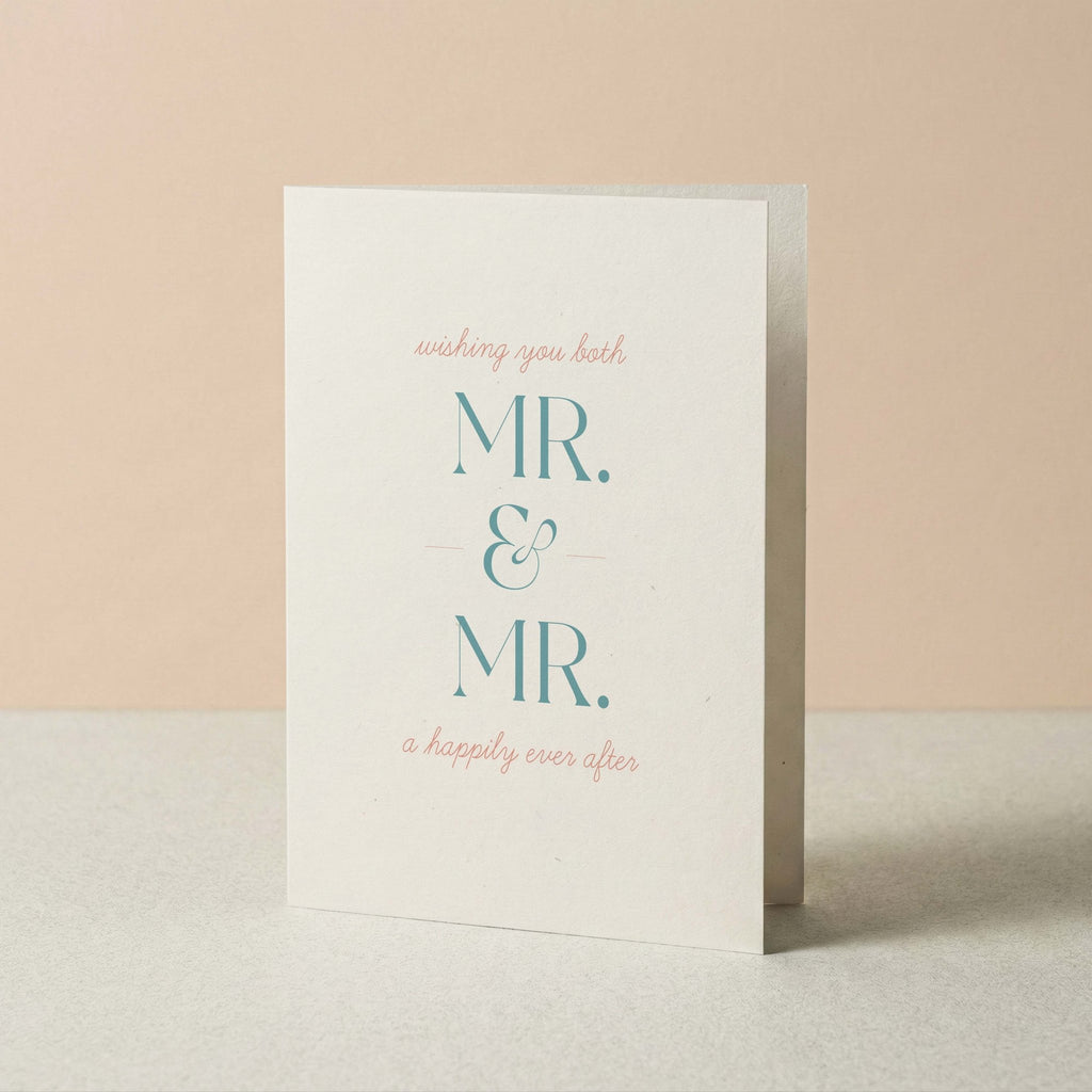 A white greeting card standing upright on a light surface against a soft peach background. The card reads 'wishing you both MR. & MR. a happily ever after.'