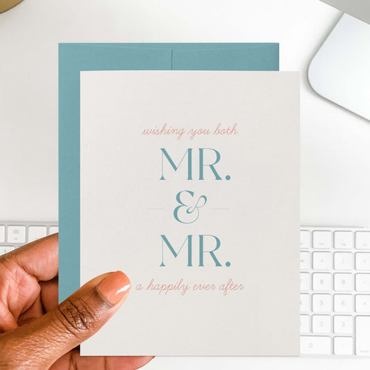 Hand holding Mr. + Mr. wedding greeting card with teal envelope behind