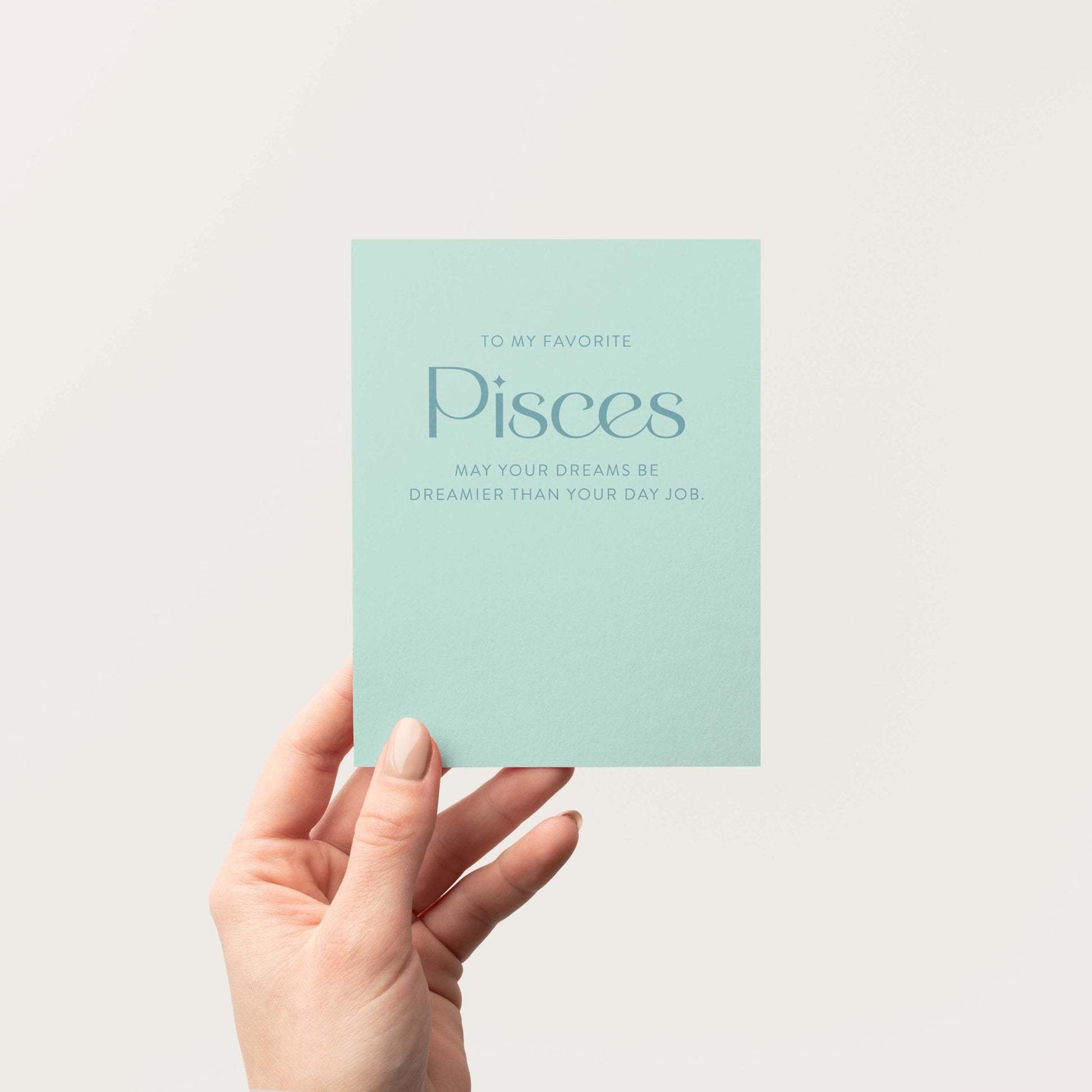 Hand holding a soft aqua-toned card with Pisces zodiac text on a white background