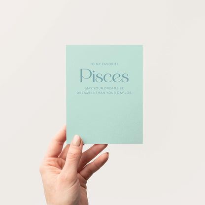 Hand holding a soft aqua-toned card with Pisces zodiac text on a white background