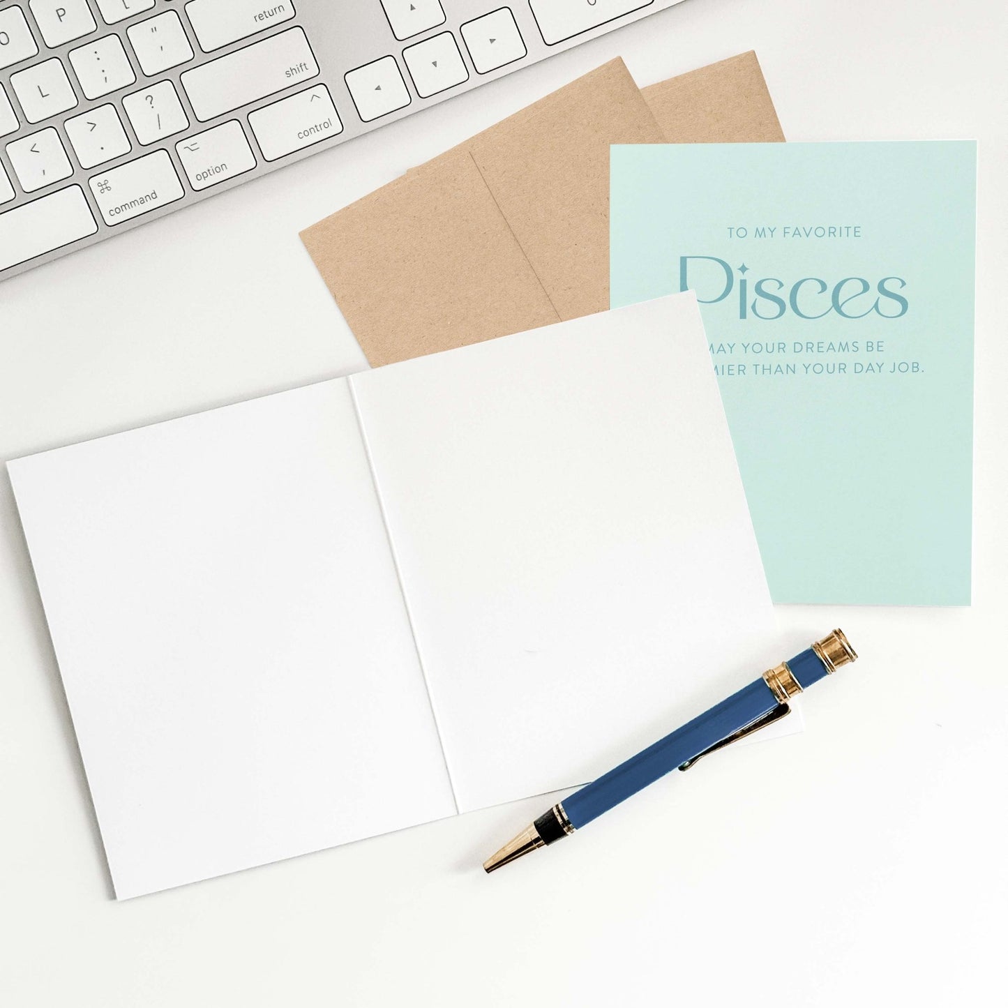 Pisces birthday card open on desk with envelope, pen, and keyboard