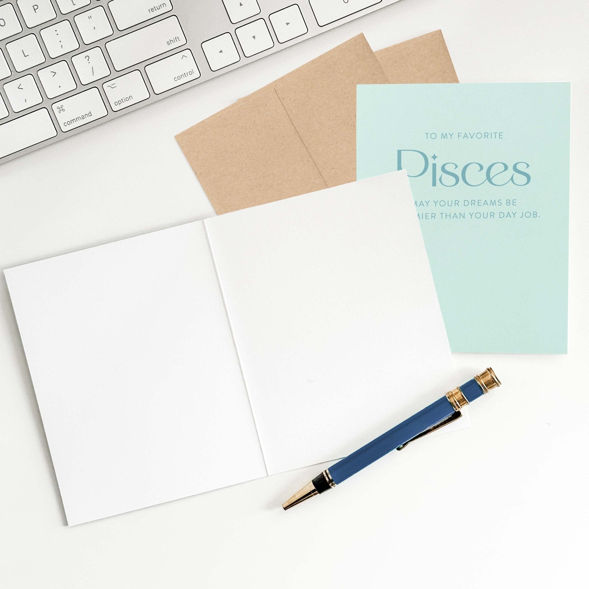Pisces birthday card open on desk with envelope, pen, and keyboard