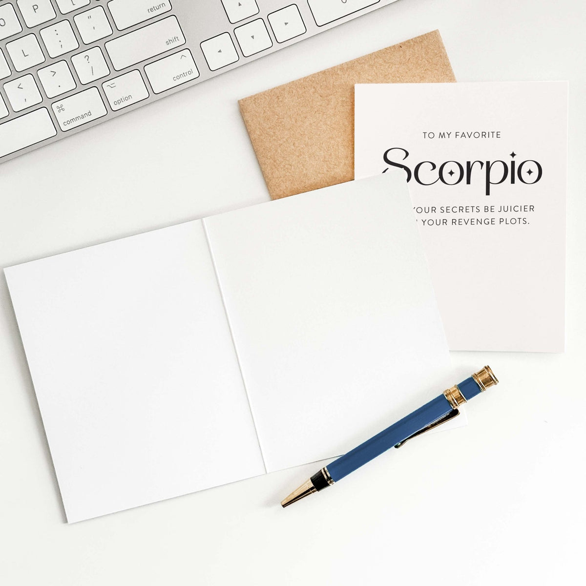 My Favorite Scorpio greeting card by Blú Rose shown open to reveal the blank interior, styled on a desk with a keyboard, kraft envelope, and blue pen