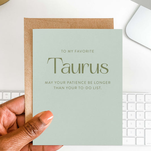 Hand holding Taurus birthday card with kraft envelope and keyboard in background