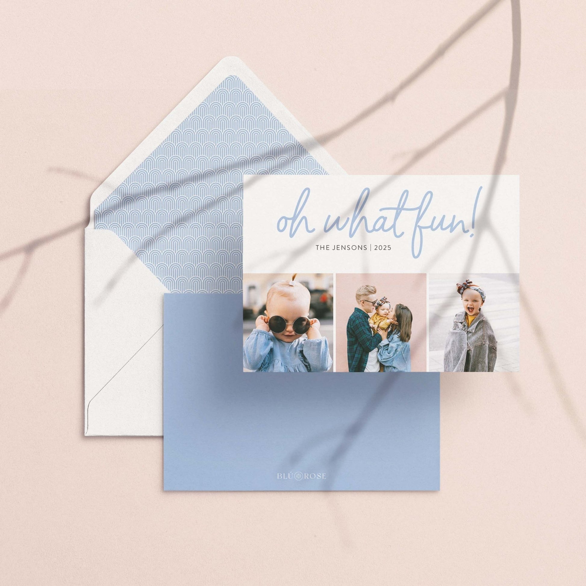 Personalized Oh What Fun holiday photo card with white envelope and matching blue pattern liner, flat lay on neutral background.