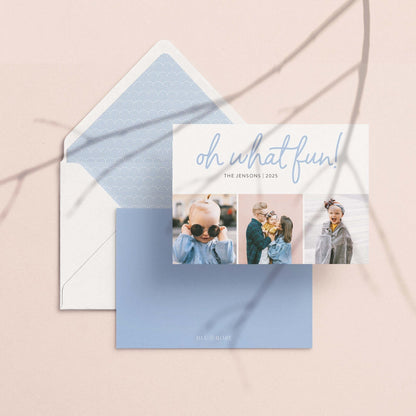 Personalized Oh What Fun holiday photo card with white envelope and matching blue pattern liner, flat lay on neutral background.