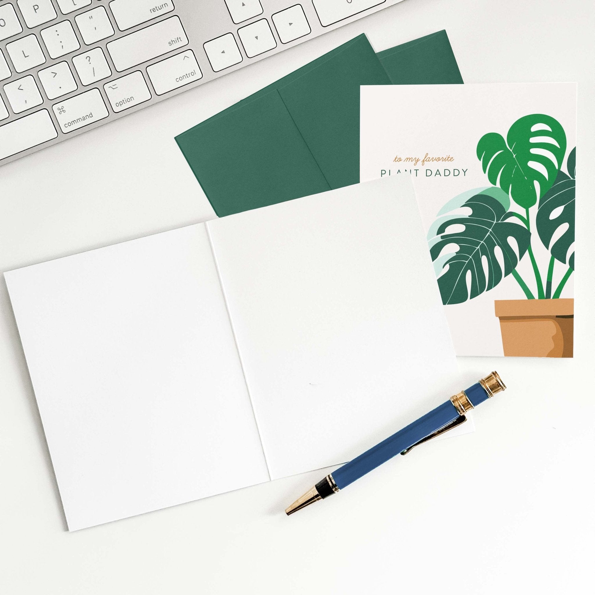 Plant Daddy card by Blú Rose shown open with blank interior, green envelope and pen on a white desk