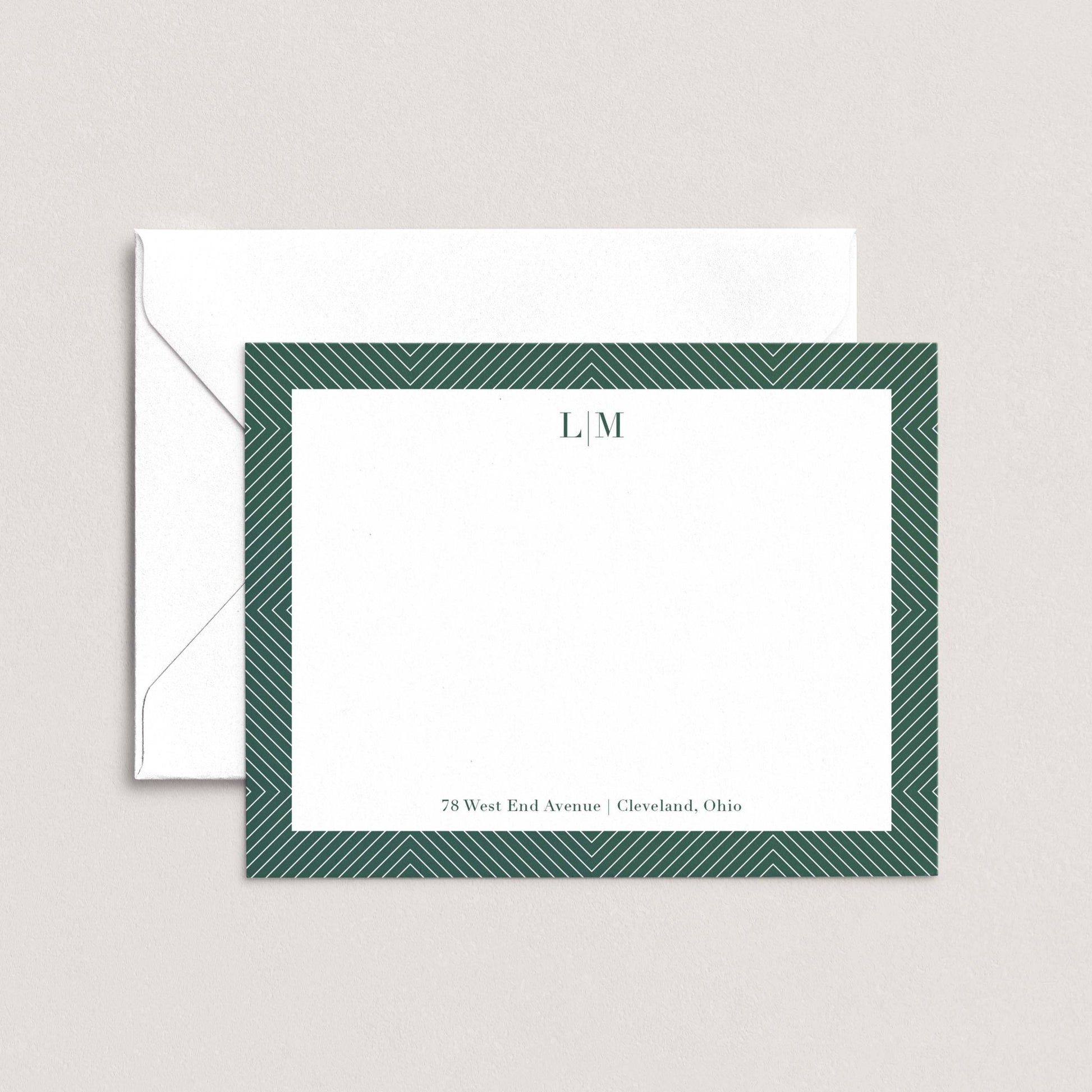 a white envelope with a green border and a blank card with a monogrammed initials on it.