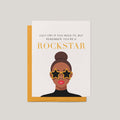 Rockstar encouragement greeting card by Blú Rose, illustration of a woman in gold star sunglasses with you're a rockstar text, shown with marigold envelope