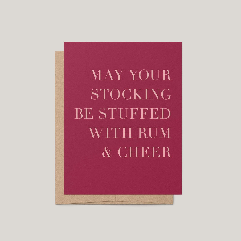 Rum + Cheer funny Christmas greeting card by Blú Rose, wine red card with blush serif text, shown with kraft envelope