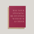 Rum + Cheer funny Christmas greeting card by Blú Rose, wine red card with blush serif text, shown with kraft envelope