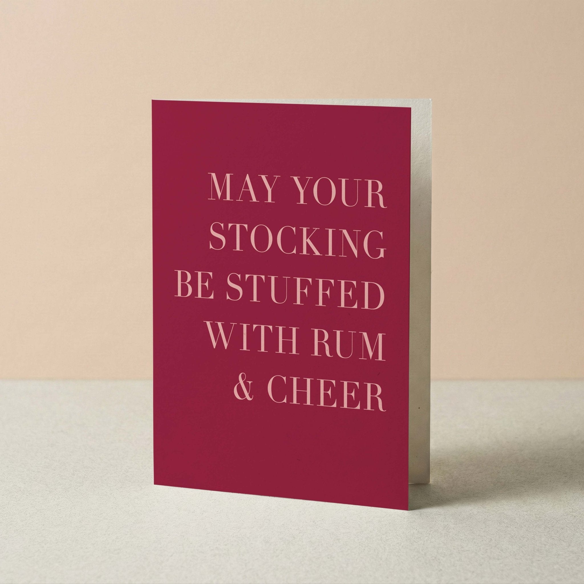 Rum + Cheer holiday card by Blú Rose standing upright, wine red card with blush typography on a neutral background
